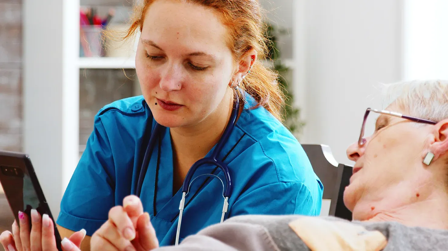 Image of nurse talking to elderly patient while showing her cell phone